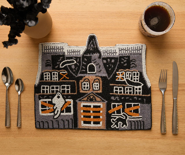 Handmade beaded haunted house placemat featuring ghost, cat, bat, and boarded window details in black, orange, and silver. Perfect for Halloween decor.