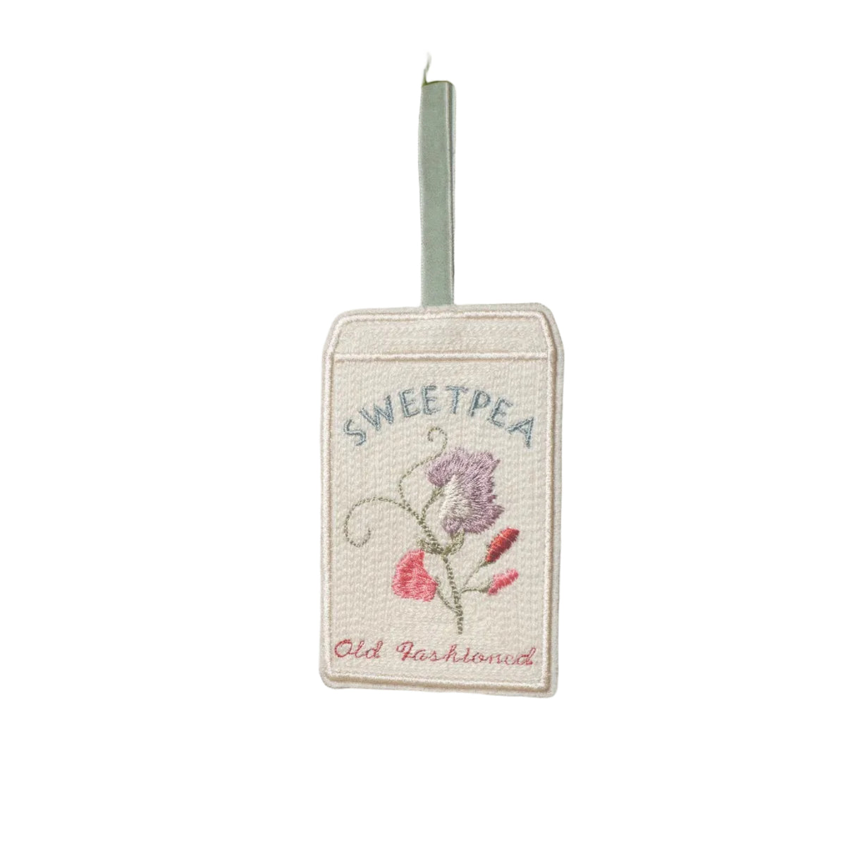 Embroidered Sweet Pea ‘Old Fashioned’ seed packet decoration hanging from a velvet ribbon amongst leafy branches in soft sunlight.