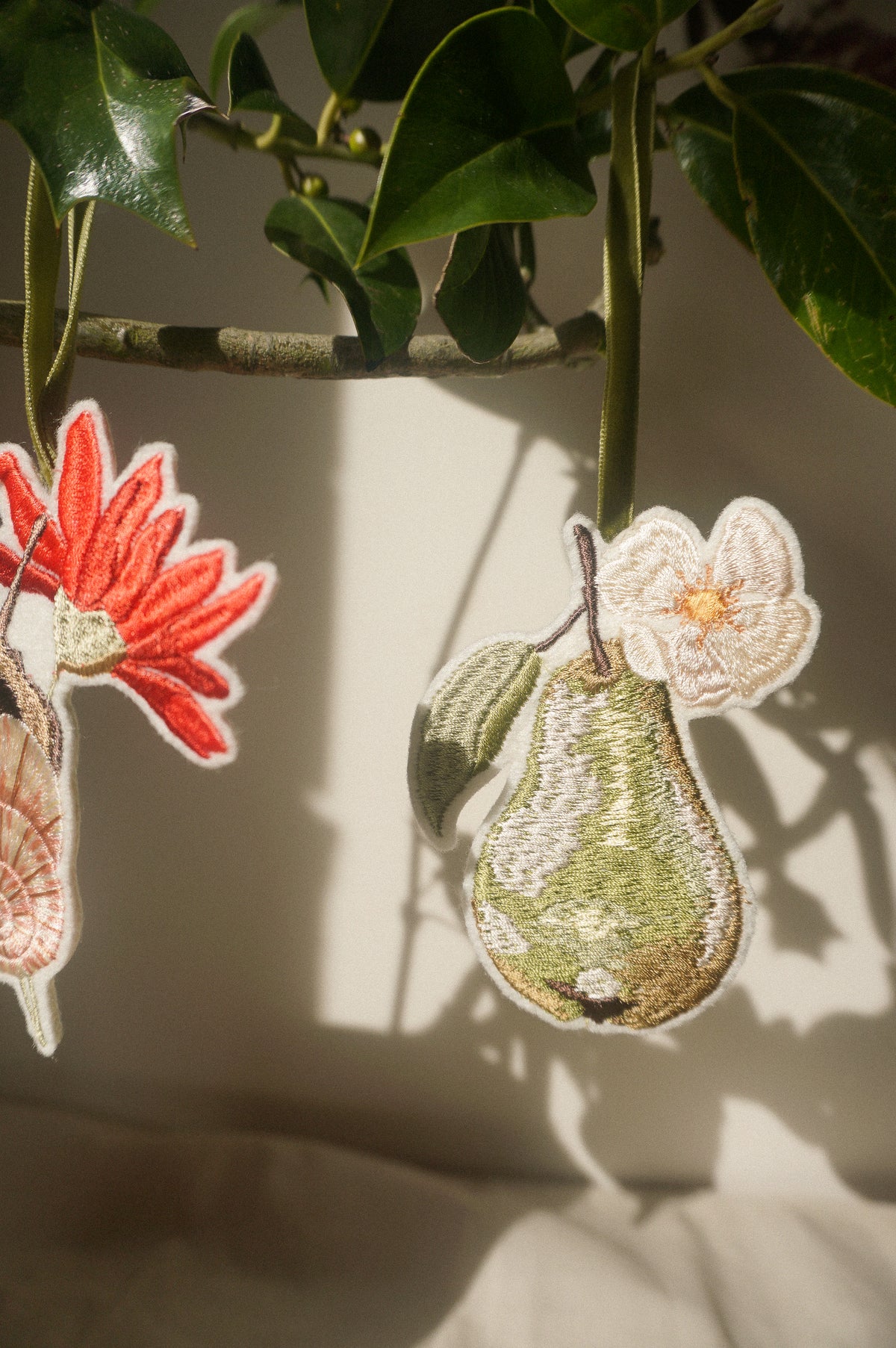 Embroidered green pear decoration with delicate white blossom and leaf, hanging from an olive green velvet ribbon.