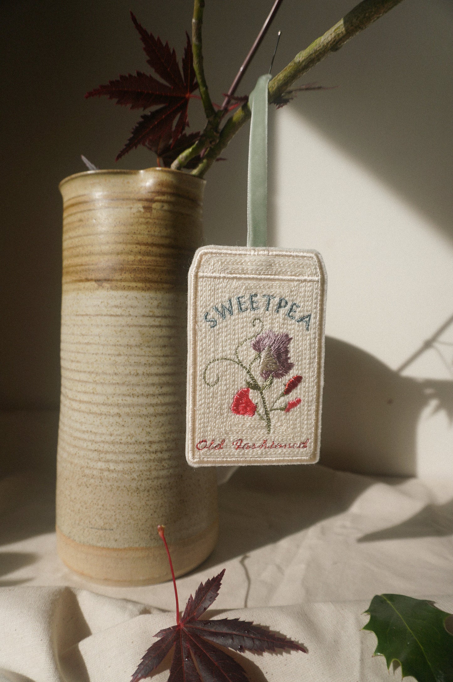 Close-up of an embroidered Sweet Pea ‘Old Fashioned’ seed packet decoration with pink and purple flowers, finished with a sage green velvet ribbon.
