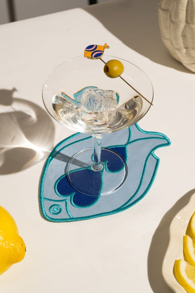 A martini with an olive rests on an Octaevo Fish Splash Coaster, beside a lemon and its fish-shaped shadow.