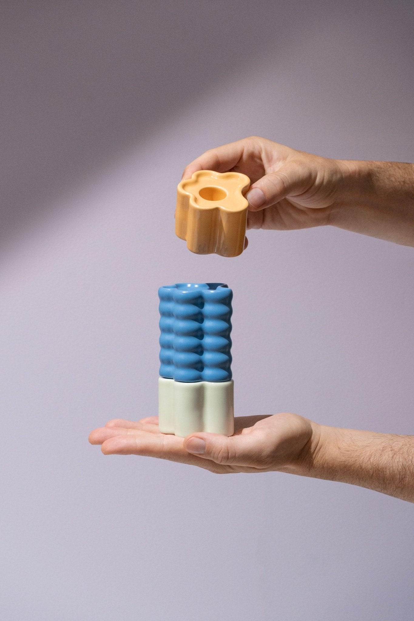 Two hands stack Octaevo Flora Candle Holder in blue, featuring colorful hand-glazed ceramics, against a light background.
