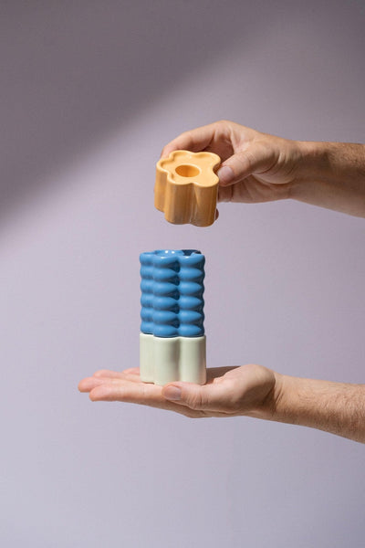 Two hands stack Octaevo Flora Candle Holder in blue, featuring colorful hand-glazed ceramics, against a light background.