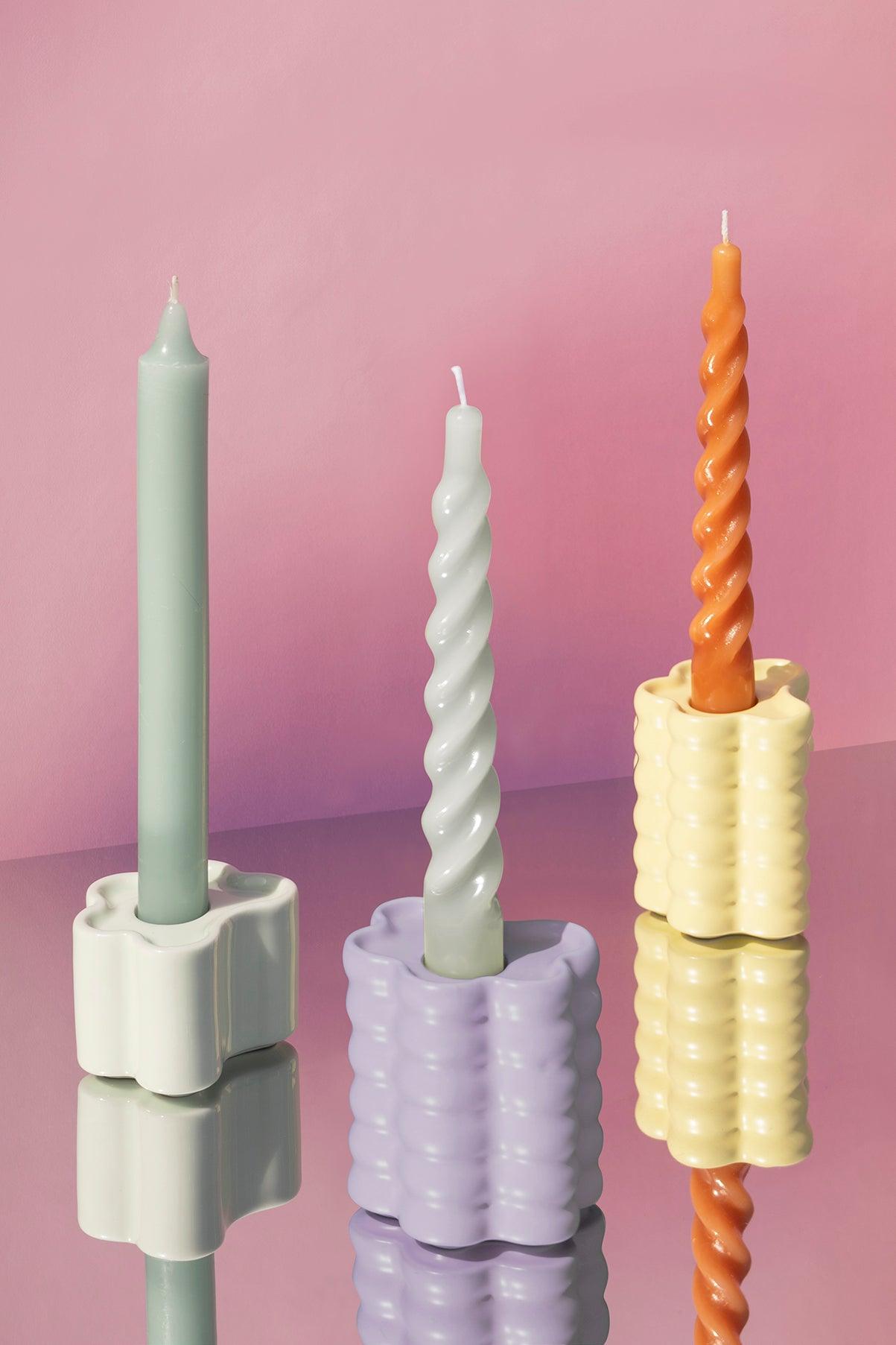 Flora Candle Holders by Octaevo with pastel candles are shown on a reflective surface against a pink background.