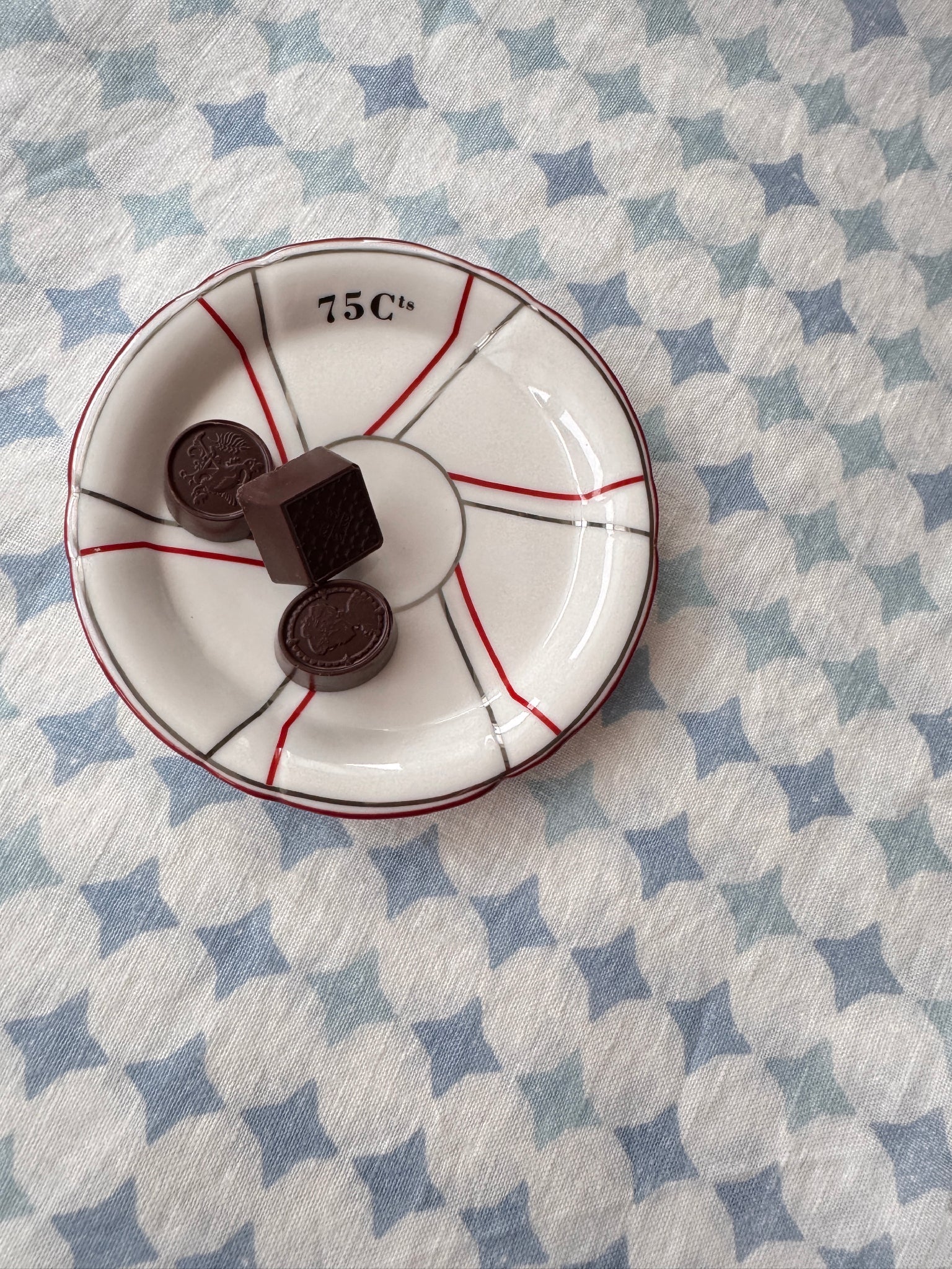 Small French white plate with red accents holding chocolate cookies on a blue and white linen tablecloth.