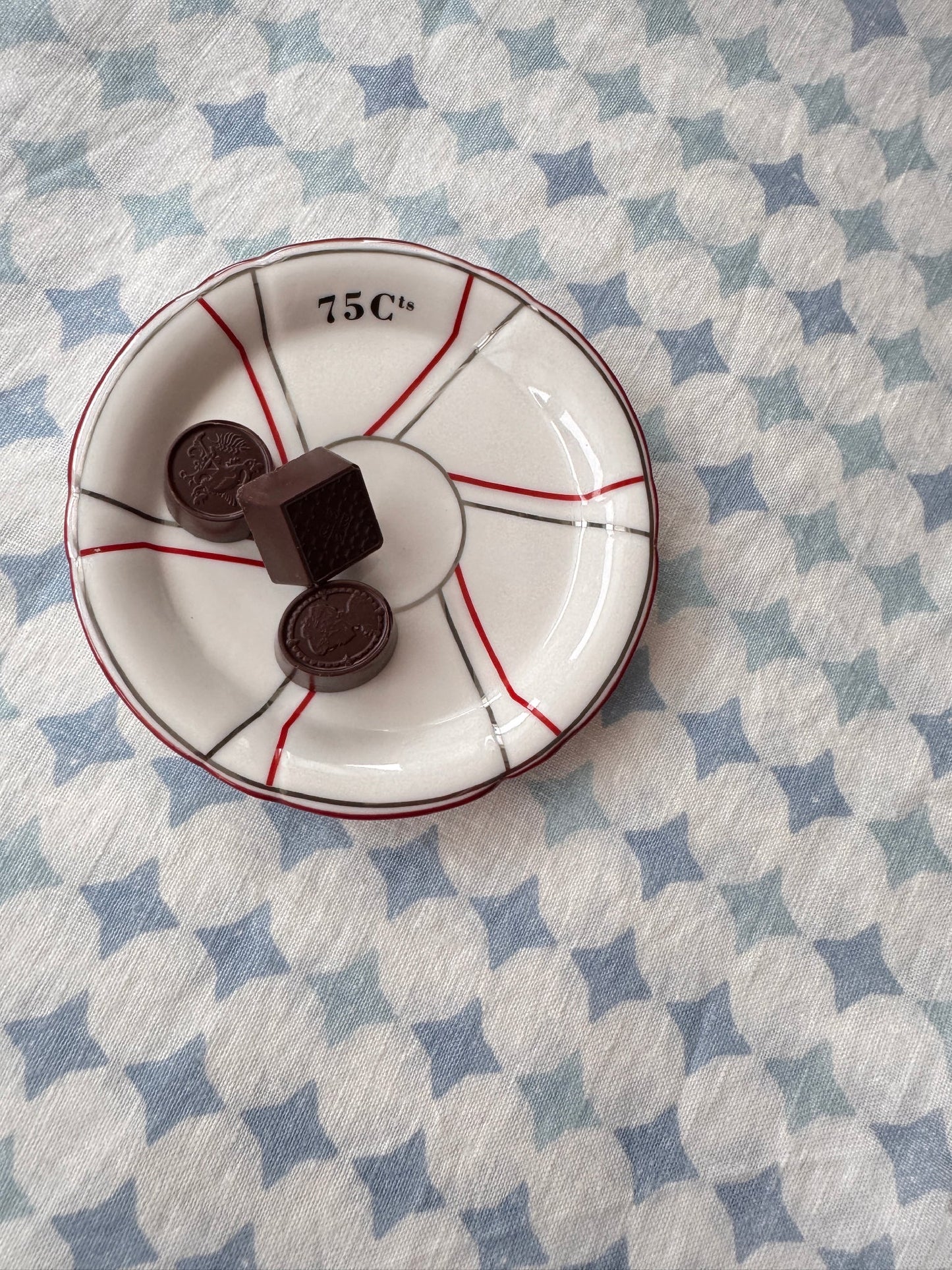 Small French white plate with red accents holding chocolate cookies on a blue and white linen tablecloth.