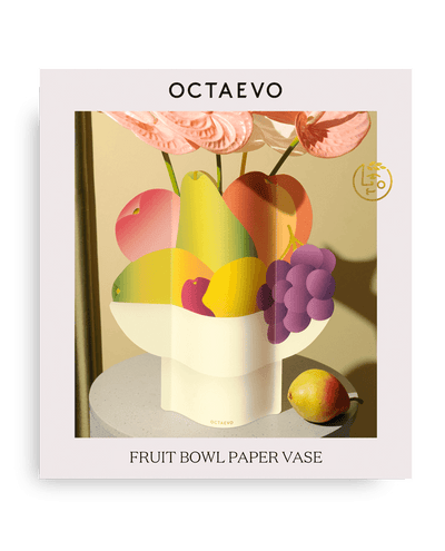 The Octaevo Fruit Bowl Paper Vase holds fruits as a centerpiece, with a pear beside it, displayed on a table.