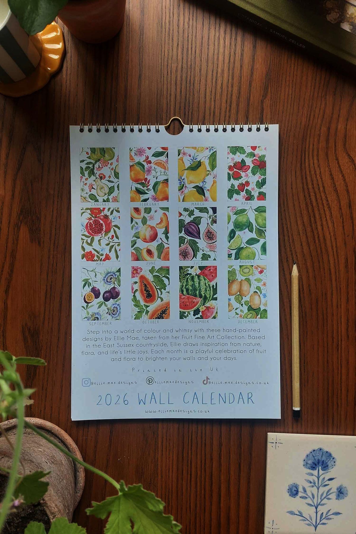 2026 wall calendar with floral and fruit designs on a wooden surface.