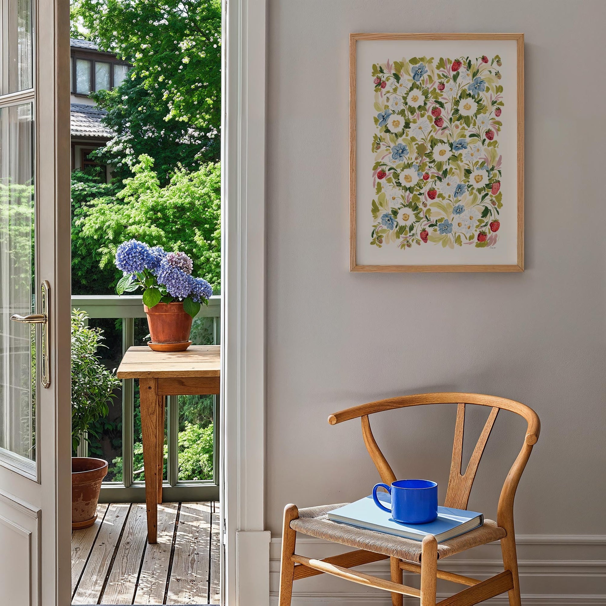 Garden Strawberries Print in light wood frame, styled A2 Print against white wall in kitchen with chair, and flower pots outside.