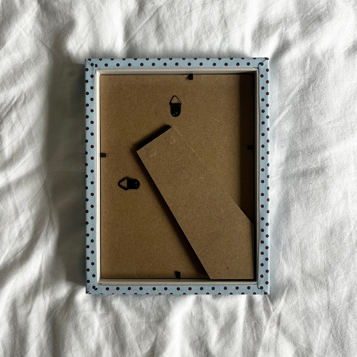 Back view of handmade blue and burgundy Pembroke polka dot fabric picture frame, showing wall fittings and frame structure