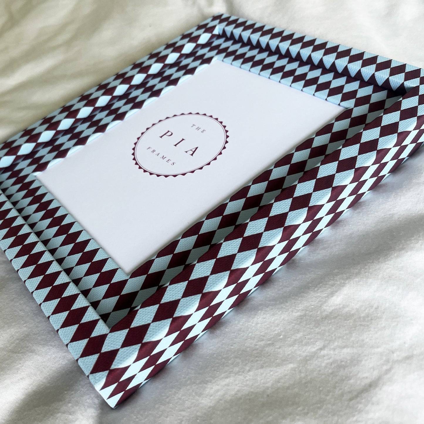 Side view of burgundy and blue harlequin fabric frame, on a white linen fabric, showcasing the depth of the frame