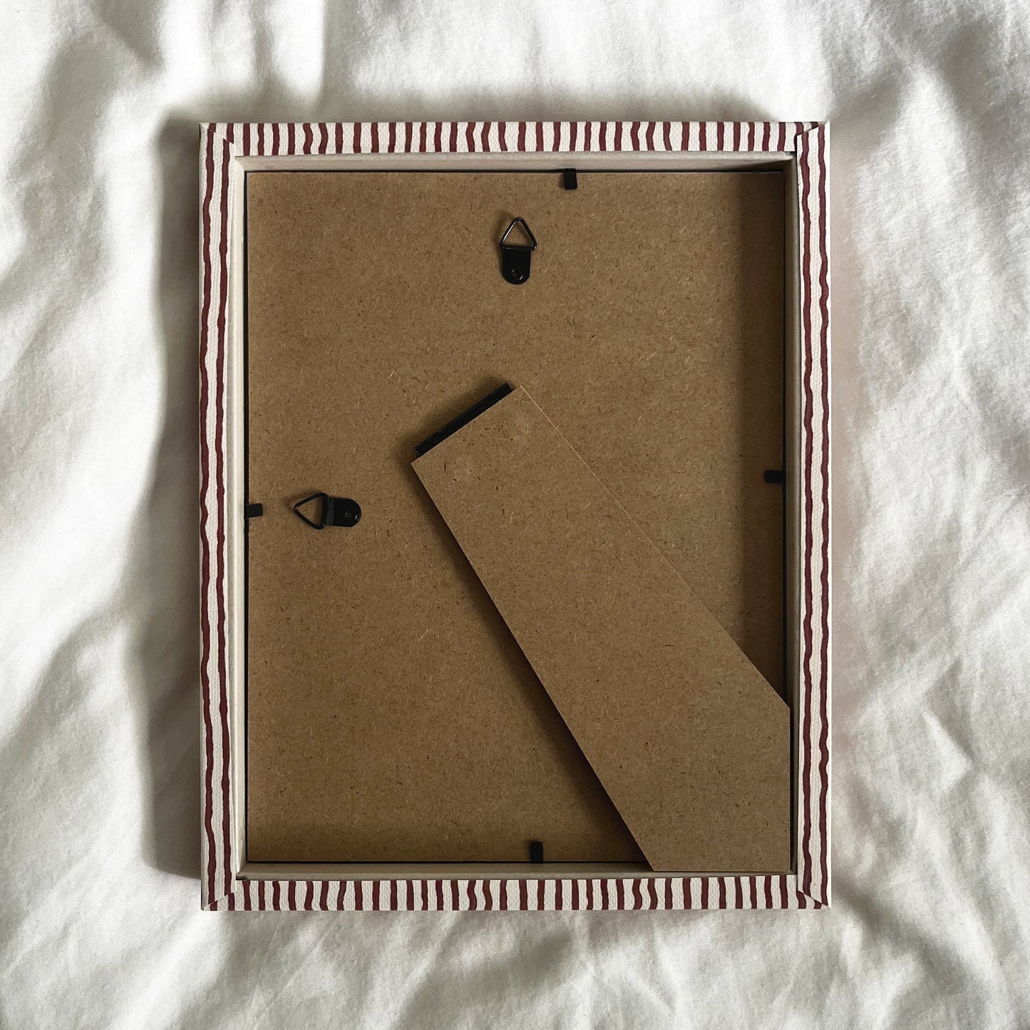 Back view of terracotta and beige striped picture frame, showing wall fittings and frame structure