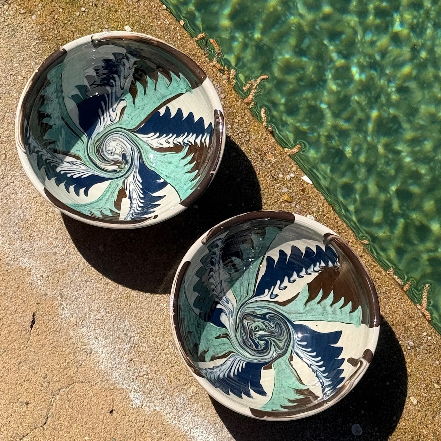 Two ceramic bowls with a decorative pattern on a sandy surface near water.-lifestule