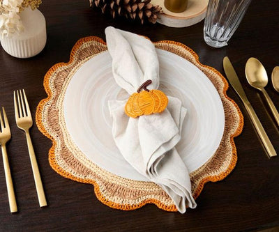 Pumpkin napkin ring holding a linen napkin on a white plate and scalloped raffia placemat