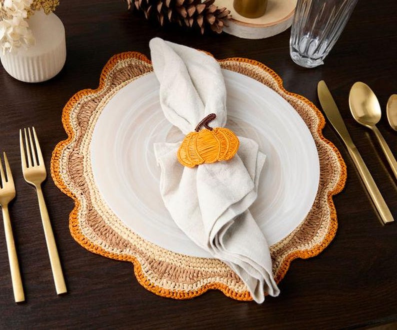Pumpkin napkin ring holding a linen napkin on a white plate and scalloped raffia placemat