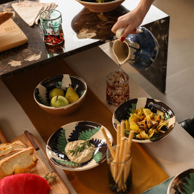 Person pouring a drink into a glass on a table with food and drinks. -lifestyle