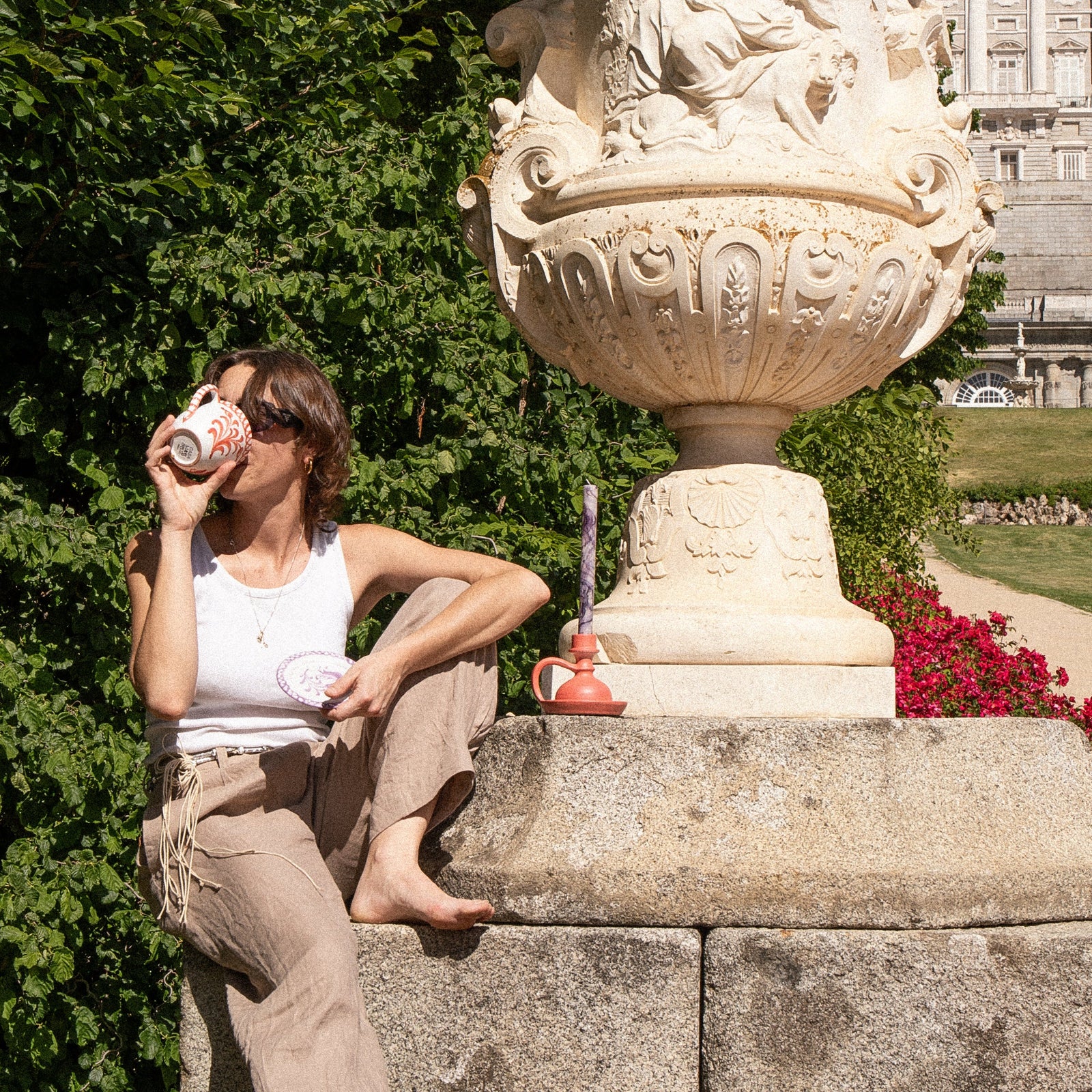 Person sitting on a large decorative stone urn in a garden with a building in the background - lifestyle