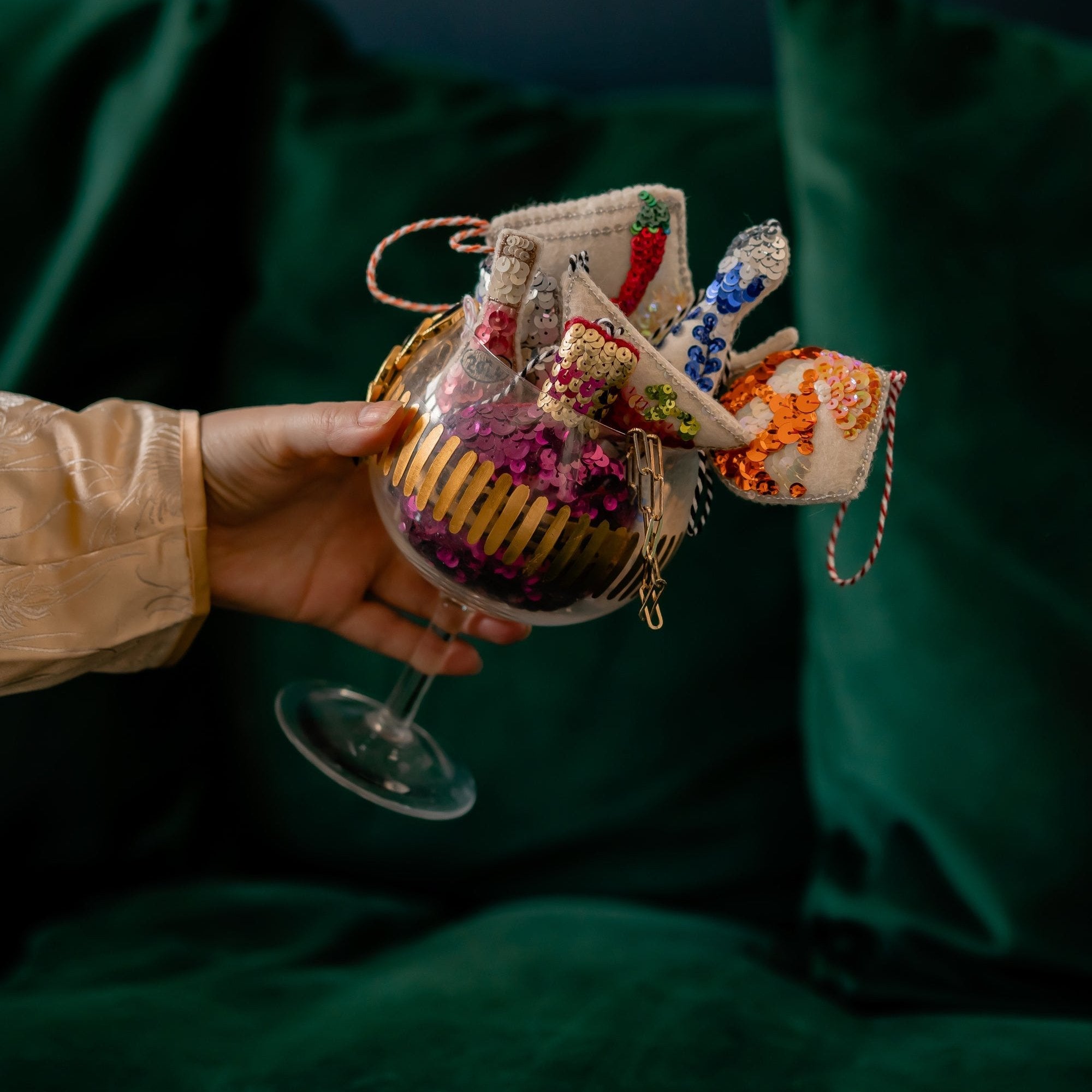 A woman's hand holding a glass filled with a selection of sequinned ornaments. 