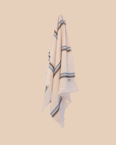 Ecru hand towel with blue stripes hanging on hook with butter yellow background
