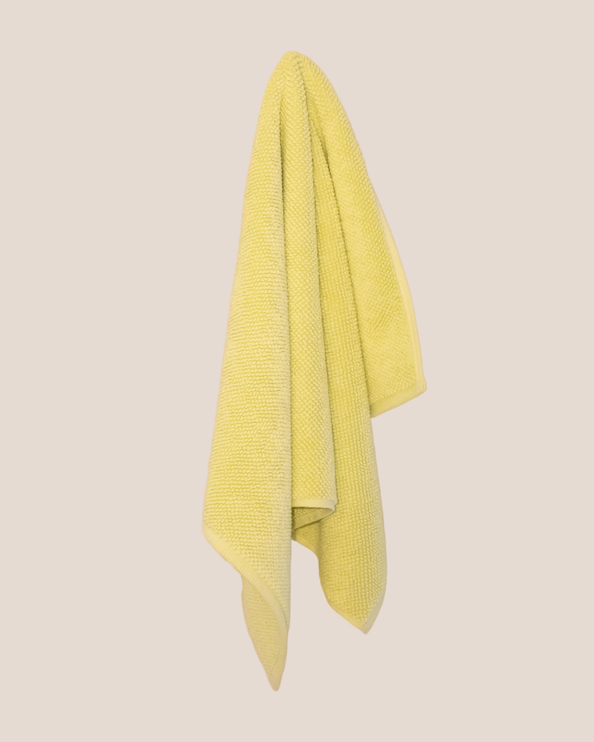 Textured yellow bathmatl hanging against a beige background