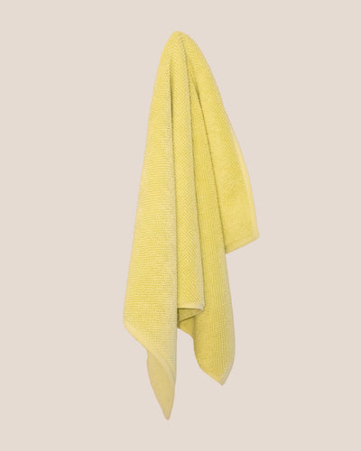 Textured yellow bathmatl hanging against a beige background