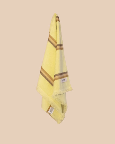 Bright yellow hand towel with brown stripes hanging on a netural wall.