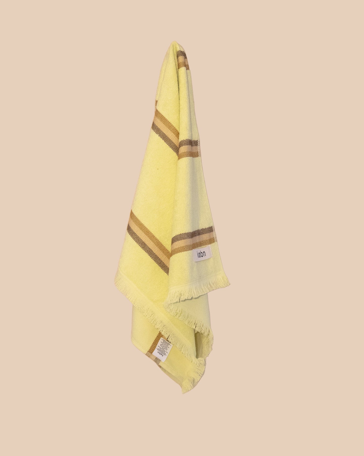 Bright yellow hand towel with brown stripes hanging on a netural wall.