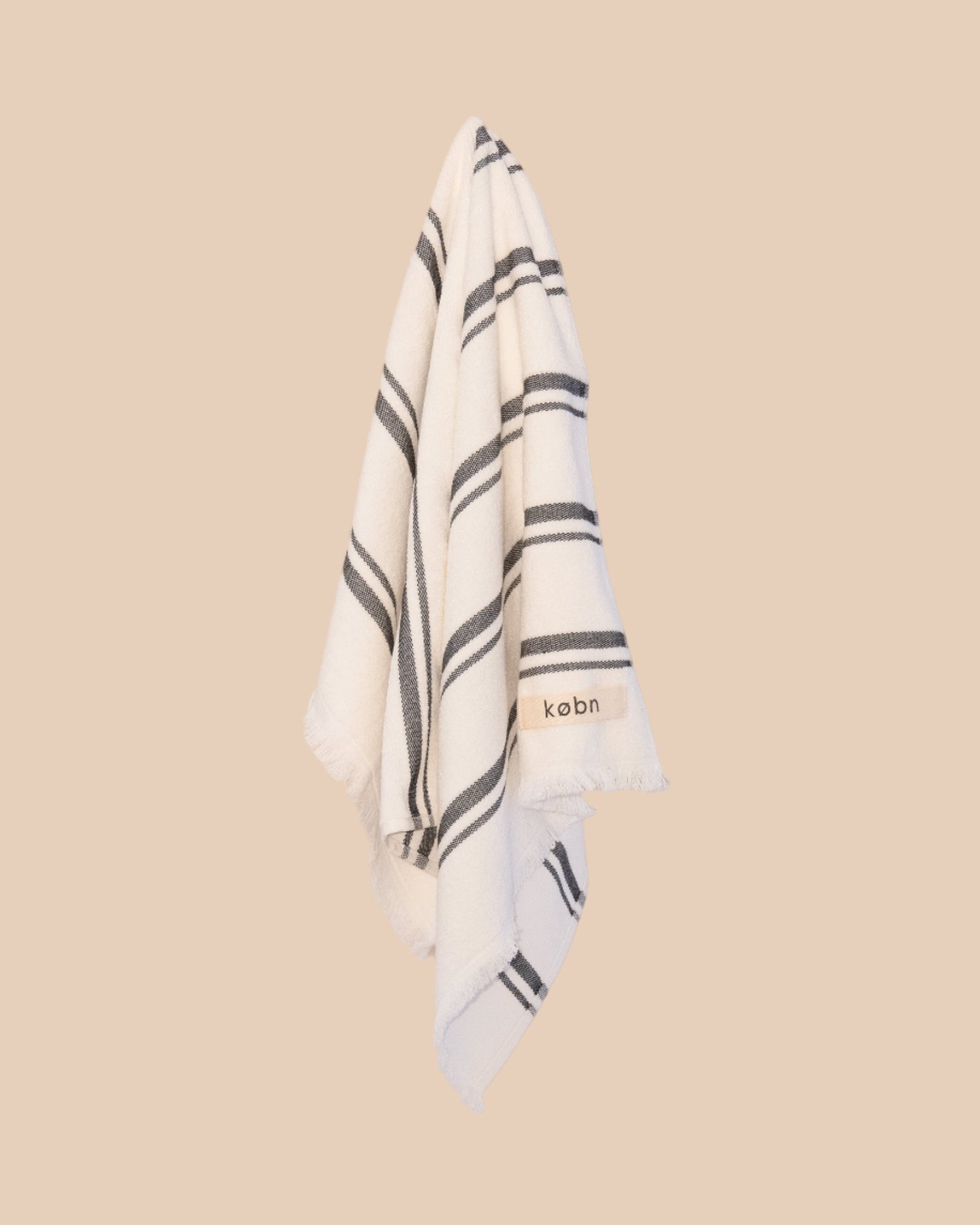 White hand towel with black stripes and 'kobn' branding on a beige background