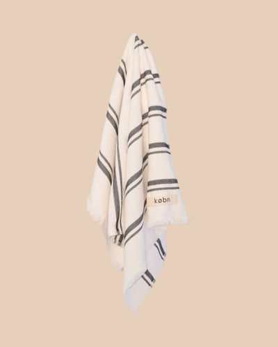 White hand towel with black stripes and 'kobn' branding on a beige background