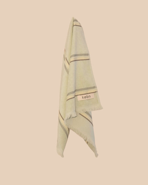 Light green hand towel with striped pattern and 'kebn' label on a beige background
