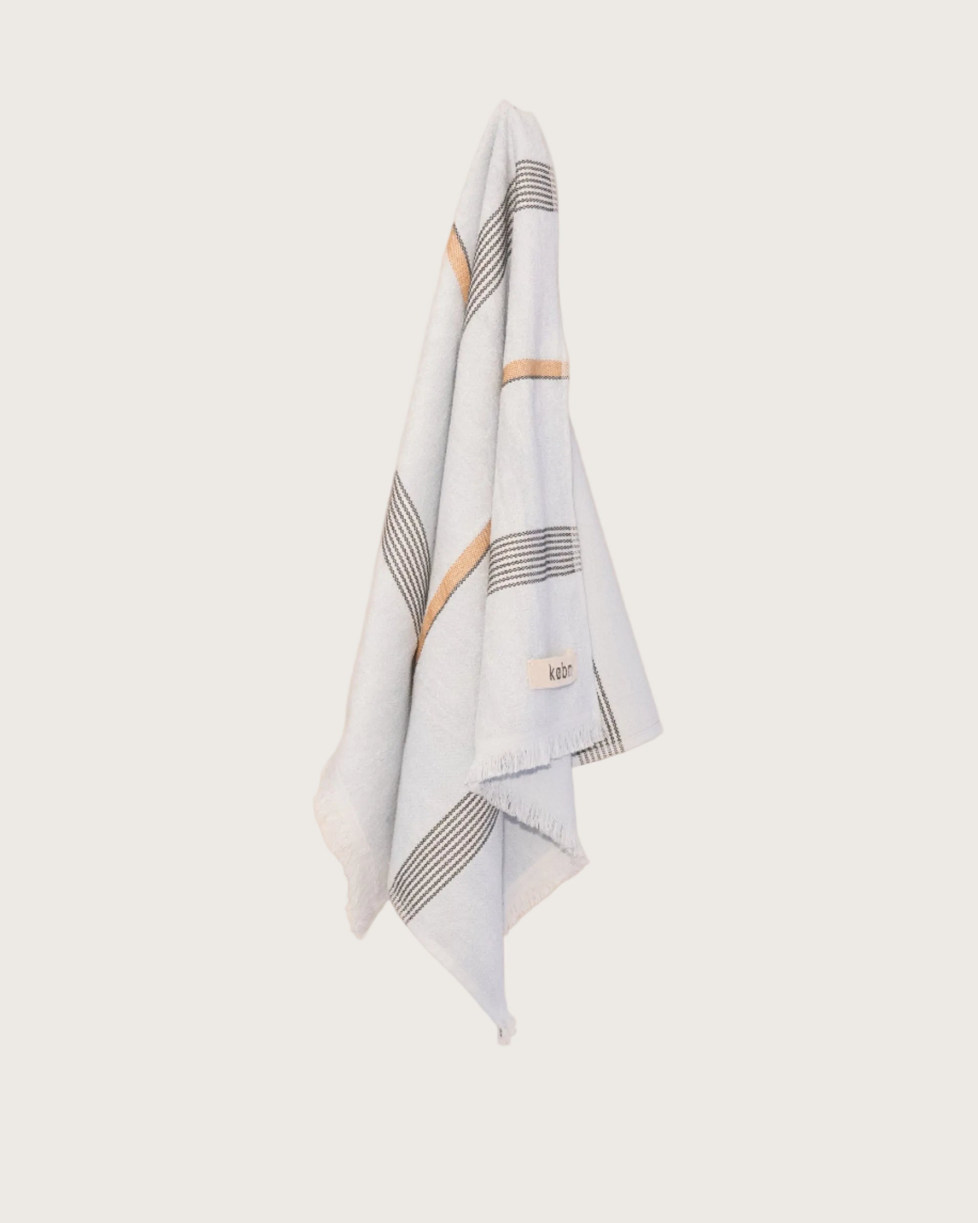 Pale Blue hand towel with stripes and fringing hanging on a butter yellow wall. 