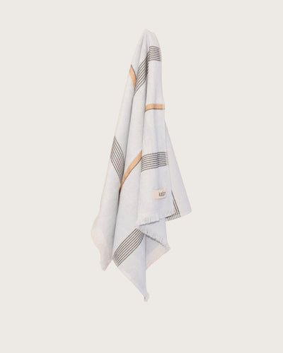 Pale Blue hand towel with stripes and fringing hanging on a butter yellow wall. 