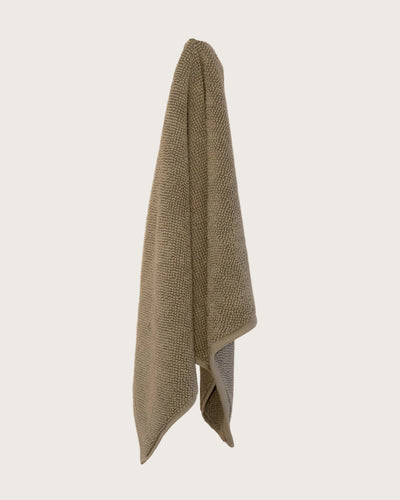 Olive coloured chunky weave cotton bahtmat hanging on a neutral background. 