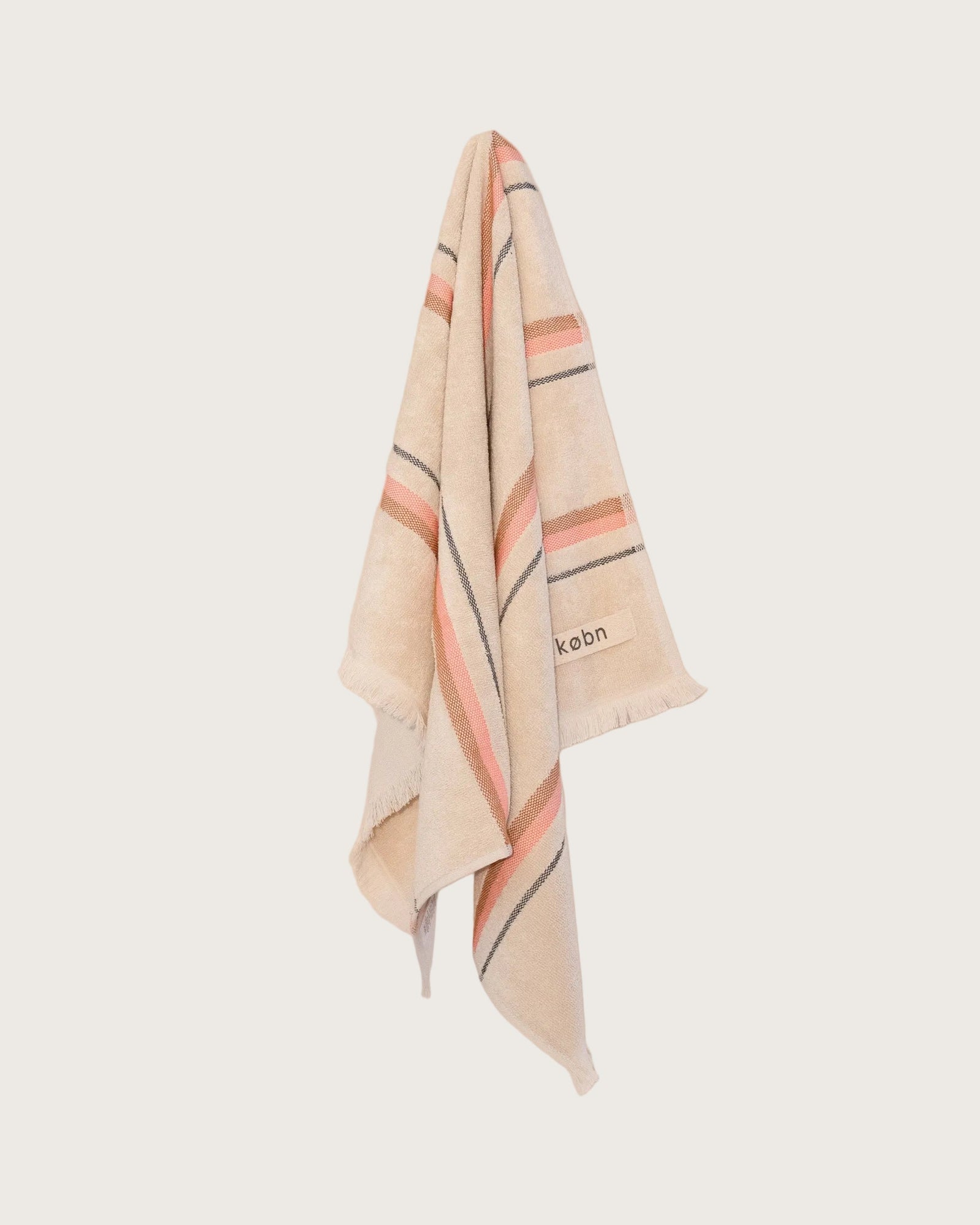striped hand towel in sand colour with a hot pink and tan stripe hanging on a neutral background. 