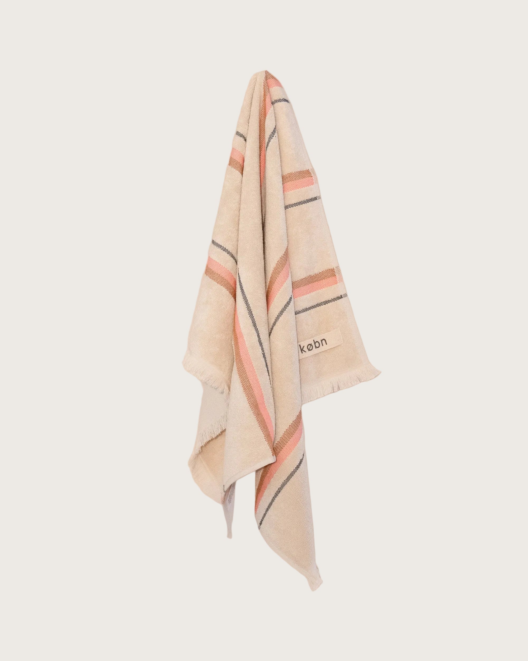 striped hand towel in sand colour with a hot pink and tan stripe hanging on a neutral background. 