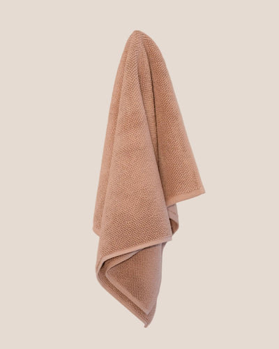 Chunky cotton weave bathmat in soft pink clay colour hanging on a butter yellow background. 