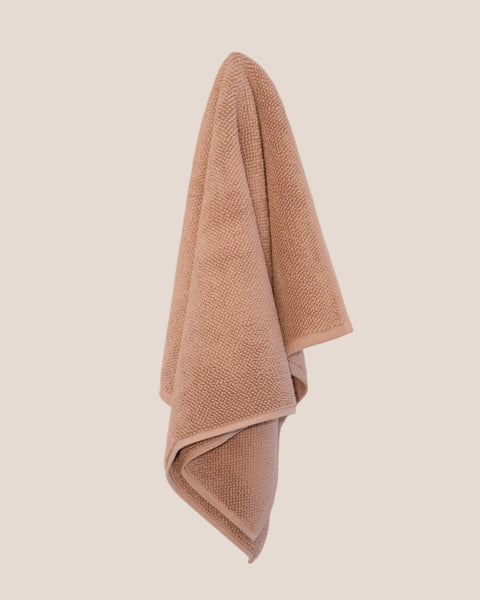 Chunky cotton weave bathmat in soft pink clay colour hanging on a butter yellow background. 