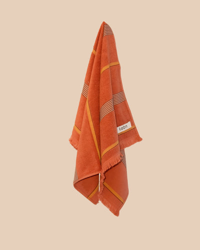 Tamarillo hand towel hanging with stripes and raw edge fringing. 