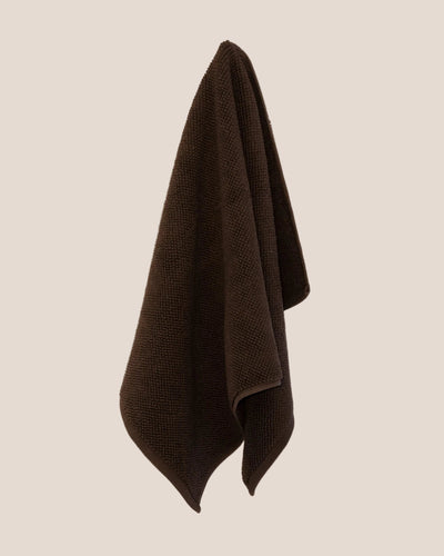 Brown textured bathmat hanging on a beige wall