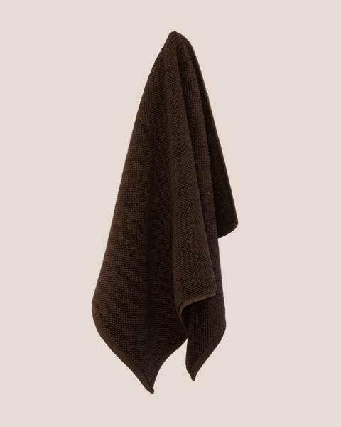Brown textured bathmat hanging on a beige wall