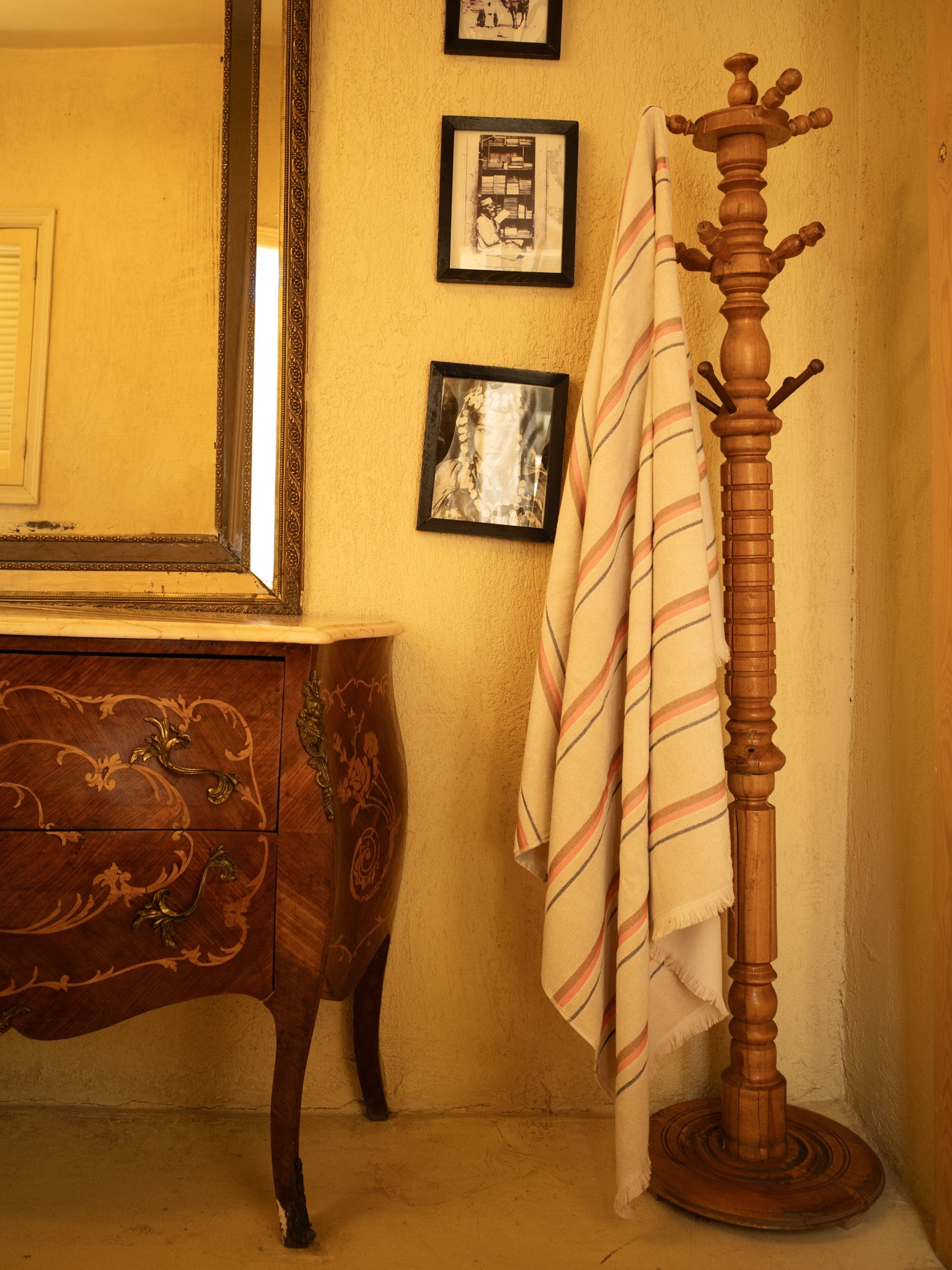 Wooden coat stand with a striped towel against a beige wall with framed pictures.
