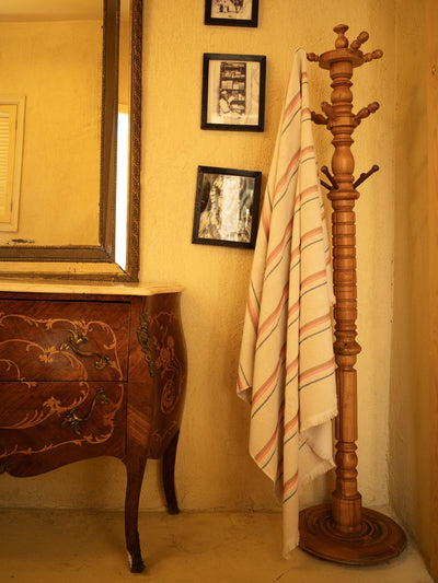 Wooden coat stand with a striped towel against a beige wall with framed pictures.