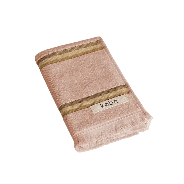 Warm pink hand towel with a tonal brown stripe, fringing and 'kobn' label on a white background