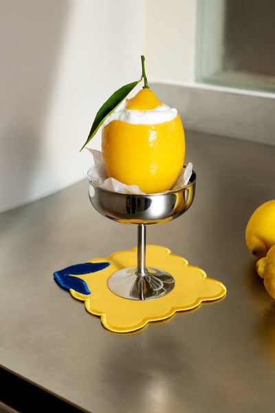 A hollowed lemon with cream sits in a metal dish on Octaevo Lemon Coasters (Set of 4), with another lemon nearby.