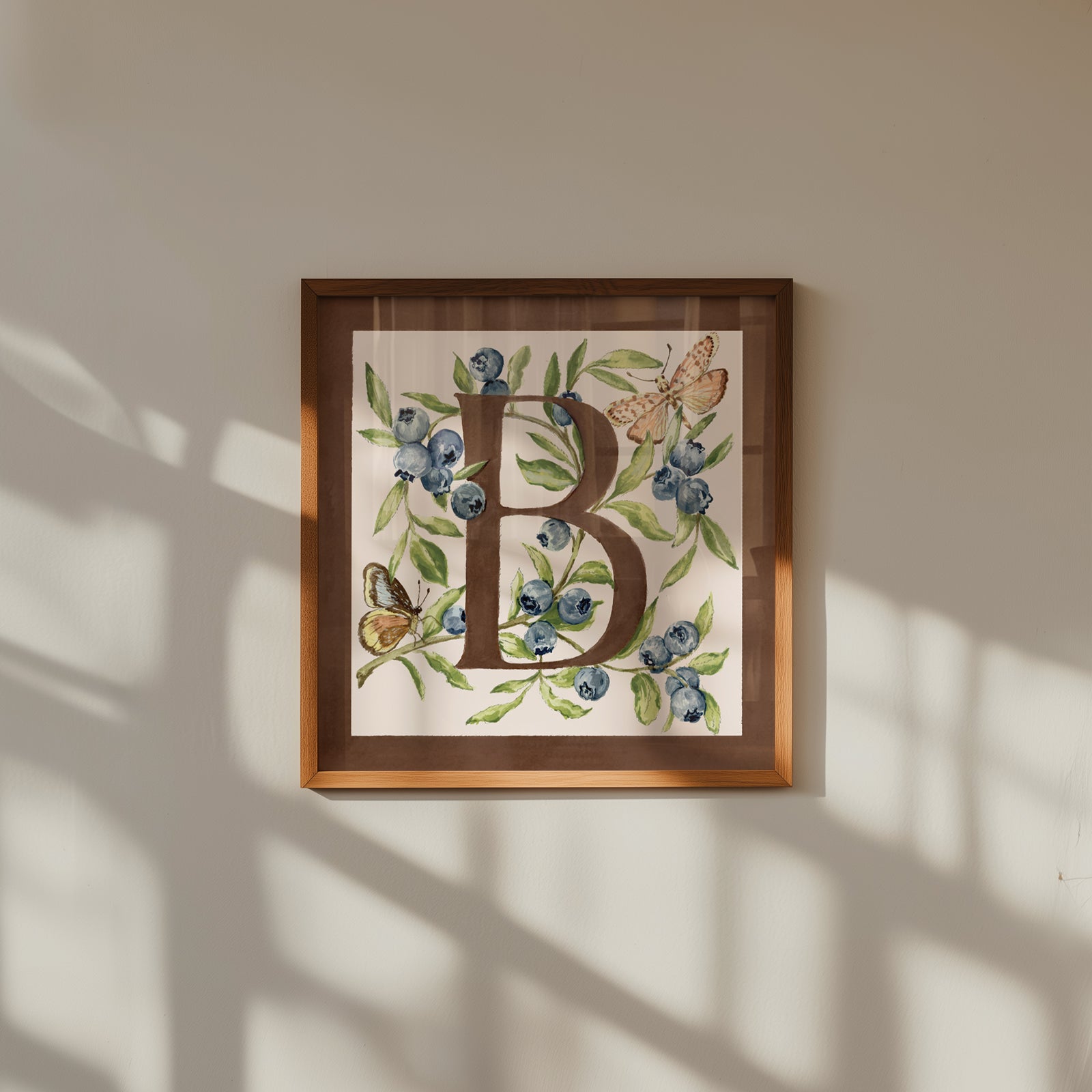 Framed artwork with letter 'B' surrounded by flowers and butterflies on a beige wall.