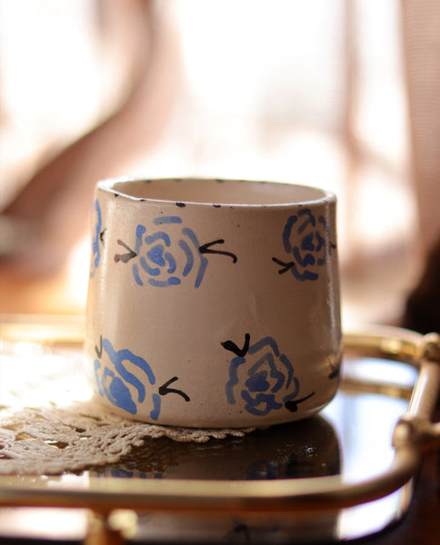 A beige ceramic mug with blue rose patterns, displayed on a table.