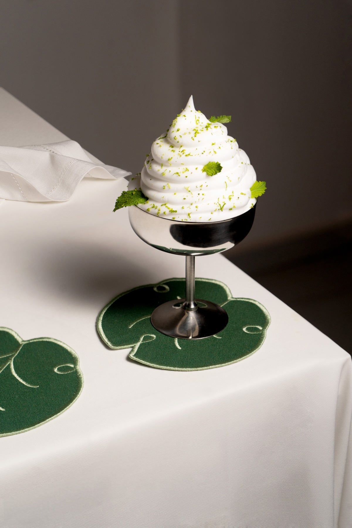 A metal cup with whipped dessert sits beside Octaevo’s Lily Leaf Coasters (Set of 4) on a white tablecloth.