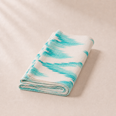 Folded blanket with turquoise and white pattern on a beige background
