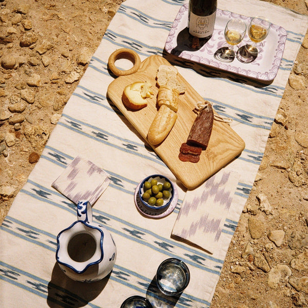 Outdoor setting with a wooden cutting board, wine, and snacks on a striped tablecloth. - lifestyle