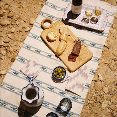 Outdoor setting with a wooden cutting board, wine, and snacks on a striped tablecloth. - lifestyle